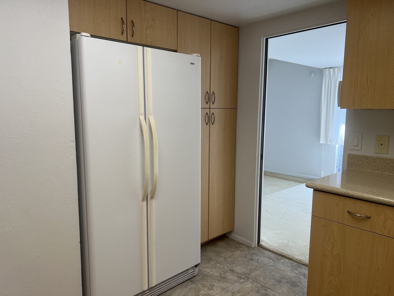 A white refrigerator with wooden cabinets beside it.